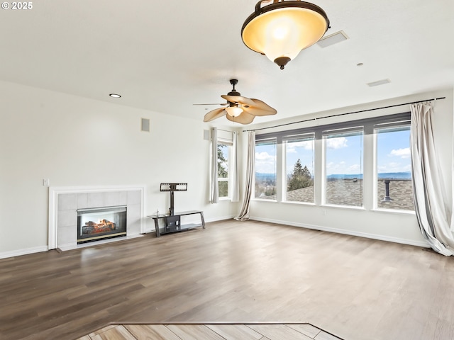 unfurnished living room featuring a tile fireplace, visible vents, baseboards, and wood finished floors