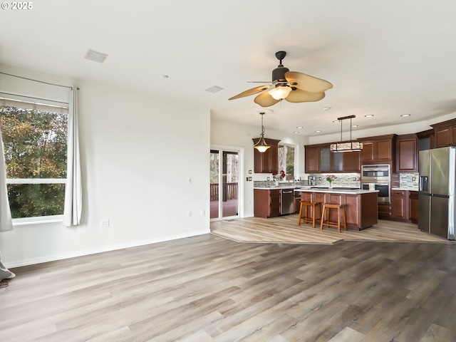 kitchen with light countertops, appliances with stainless steel finishes, a kitchen island, ceiling fan, and light wood-type flooring