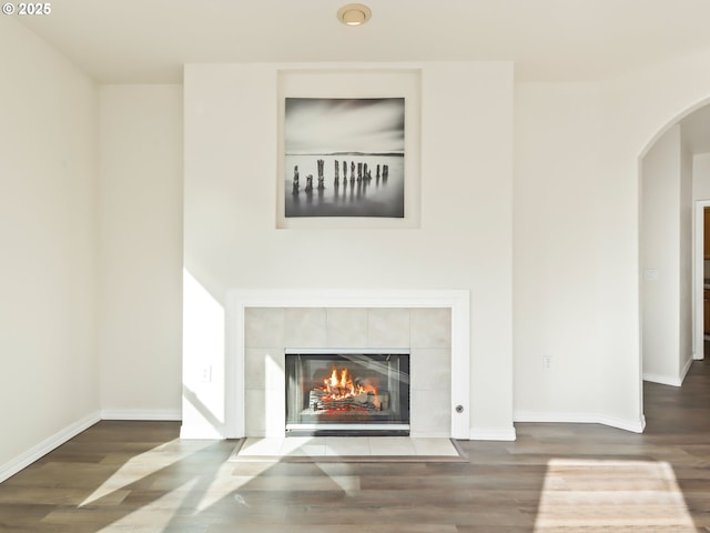 interior space featuring a fireplace, baseboards, arched walkways, and wood finished floors