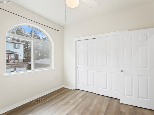 unfurnished bedroom featuring a closet, visible vents, baseboards, and wood finished floors