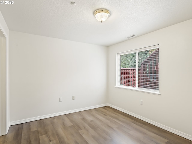 spare room with a textured ceiling, baseboards, and wood finished floors