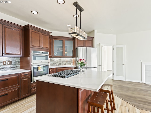 kitchen with decorative backsplash, appliances with stainless steel finishes, light countertops, a kitchen bar, and pendant lighting