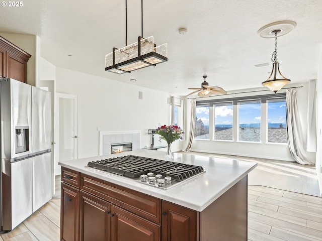 kitchen featuring a tile fireplace, light countertops, appliances with stainless steel finishes, wood tiled floor, and decorative light fixtures