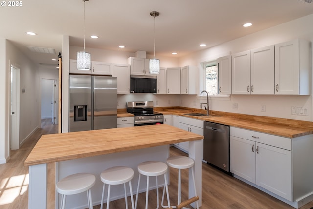 kitchen with wooden counters, appliances with stainless steel finishes, a sink, wood finished floors, and a kitchen breakfast bar