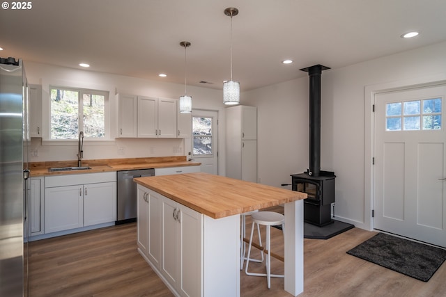 kitchen featuring a sink, wooden counters, appliances with stainless steel finishes, a kitchen bar, and a wood stove