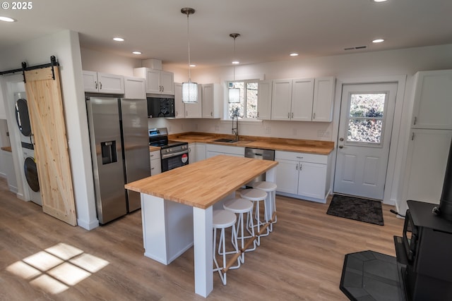 kitchen with a barn door, stacked washer and clothes dryer, butcher block counters, appliances with stainless steel finishes, and a breakfast bar area