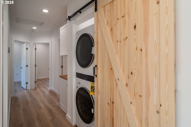 washroom featuring a barn door, recessed lighting, stacked washer and dryer, laundry area, and wood finished floors