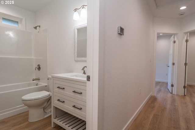 bathroom with toilet, vanity, shower / tub combination, wood finished floors, and baseboards