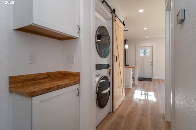 clothes washing area featuring stacked washer and dryer, a barn door, laundry area, light wood finished floors, and recessed lighting