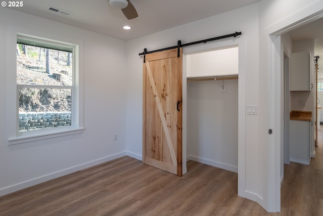 unfurnished bedroom featuring a barn door, wood finished floors, visible vents, baseboards, and a closet