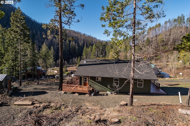 back of property featuring a forest view and roof with shingles