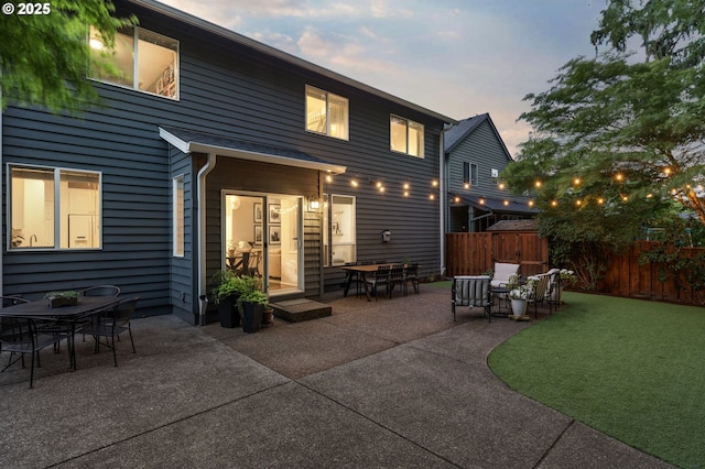 back of house at dusk featuring a patio, outdoor dining area, and fence