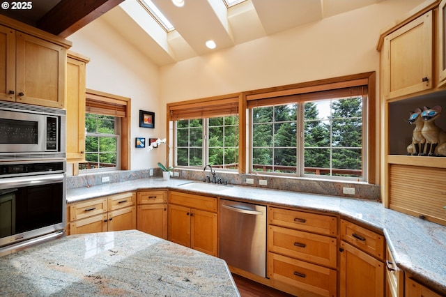 kitchen featuring appliances with stainless steel finishes, vaulted ceiling with skylight, a healthy amount of sunlight, and sink