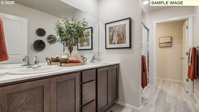 bathroom featuring double vanity, wood finished floors, a stall shower, and a sink