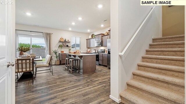 kitchen featuring dark brown cabinetry, dark wood-type flooring, stainless steel appliances, a kitchen breakfast bar, and a kitchen island