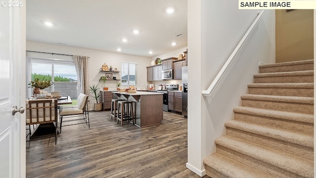 kitchen featuring a kitchen bar, dark wood-type flooring, a center island, recessed lighting, and appliances with stainless steel finishes