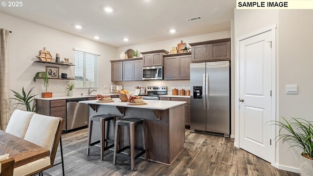 kitchen featuring a kitchen bar, appliances with stainless steel finishes, dark brown cabinetry, a center island, and dark hardwood / wood-style floors