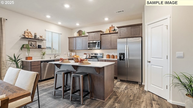 kitchen featuring a kitchen island, dark wood finished floors, light countertops, appliances with stainless steel finishes, and a kitchen breakfast bar