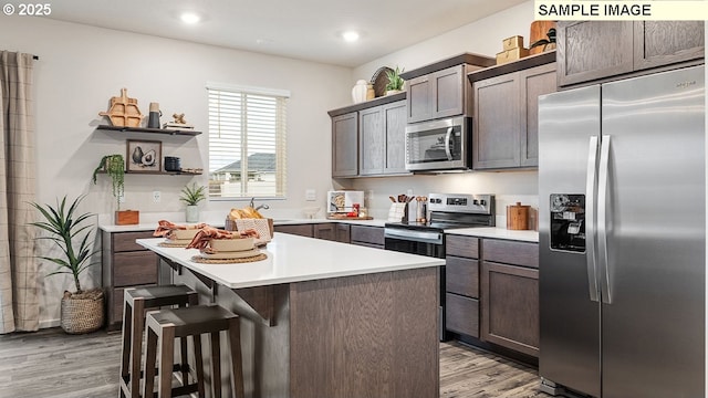 kitchen with a kitchen bar, dark brown cabinets, light hardwood / wood-style floors, and appliances with stainless steel finishes