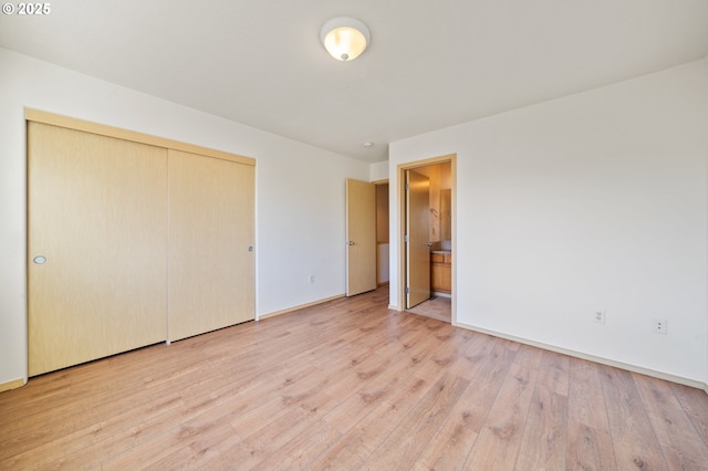 unfurnished bedroom featuring ensuite bath, a closet, and light wood-type flooring