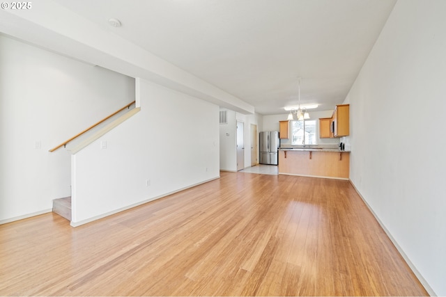 unfurnished living room with a chandelier and light wood-type flooring