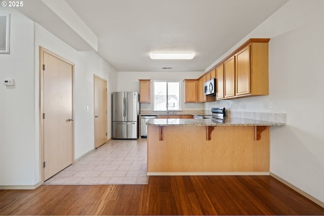 kitchen with a breakfast bar, kitchen peninsula, stainless steel appliances, light stone countertops, and light wood-type flooring