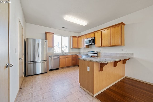 kitchen with sink, a kitchen breakfast bar, stainless steel appliances, light stone counters, and kitchen peninsula