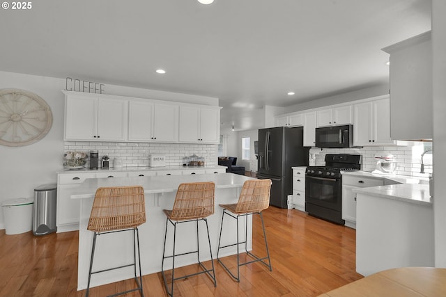 kitchen with white cabinetry, light wood-type flooring, a kitchen island, and black appliances