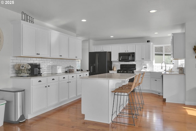 kitchen featuring white cabinetry, a kitchen breakfast bar, a center island, black appliances, and light hardwood / wood-style flooring