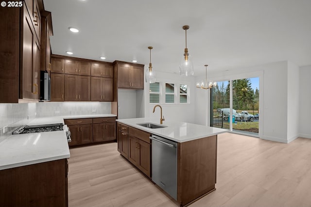 kitchen featuring stainless steel dishwasher, sink, an inviting chandelier, hanging light fixtures, and an island with sink