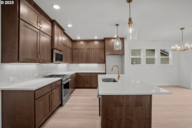 kitchen featuring sink, hanging light fixtures, light stone countertops, an island with sink, and appliances with stainless steel finishes