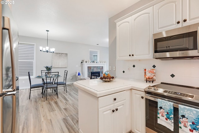 kitchen with decorative backsplash, stainless steel appliances, a tile fireplace, white cabinetry, and hanging light fixtures