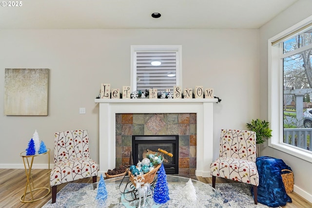 living area with wood-type flooring, plenty of natural light, and a tiled fireplace