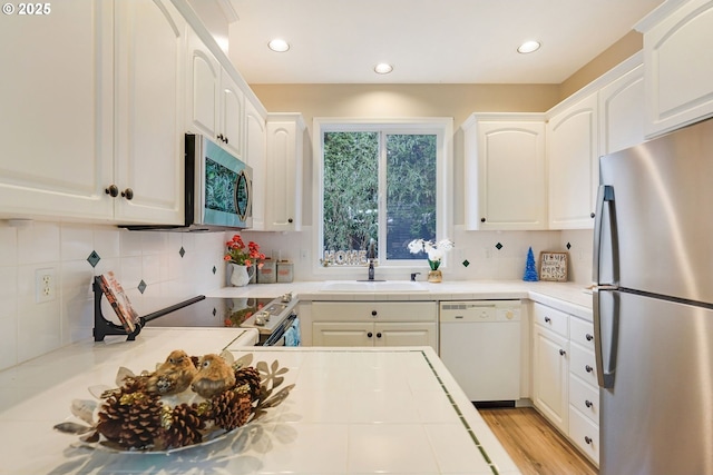 kitchen with decorative backsplash, appliances with stainless steel finishes, light wood-type flooring, sink, and white cabinetry