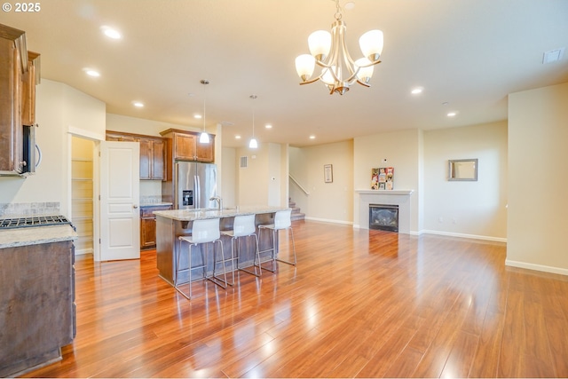 kitchen featuring light wood finished floors, appliances with stainless steel finishes, a kitchen breakfast bar, and a glass covered fireplace