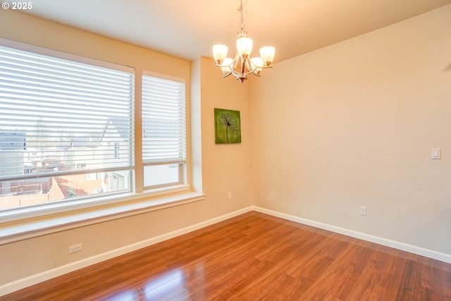 unfurnished room with baseboards, wood finished floors, and an inviting chandelier