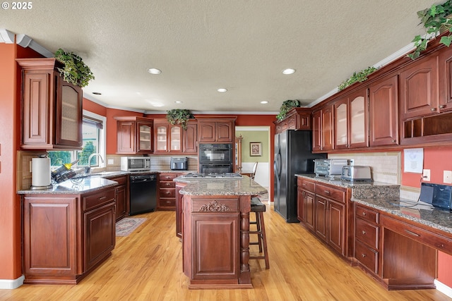 kitchen with a sink, a kitchen breakfast bar, light wood-style flooring, glass insert cabinets, and black appliances