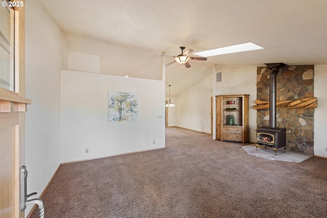 unfurnished living room featuring visible vents, ceiling fan, a wood stove, a textured ceiling, and carpet flooring