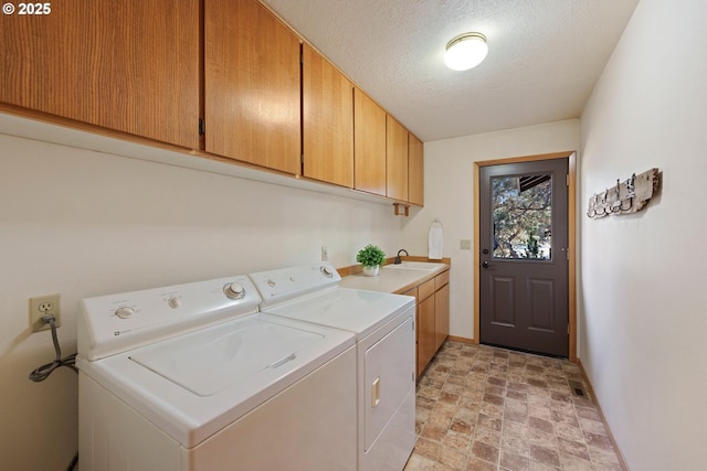 laundry room with washing machine and clothes dryer, cabinet space, stone finish flooring, a textured ceiling, and baseboards