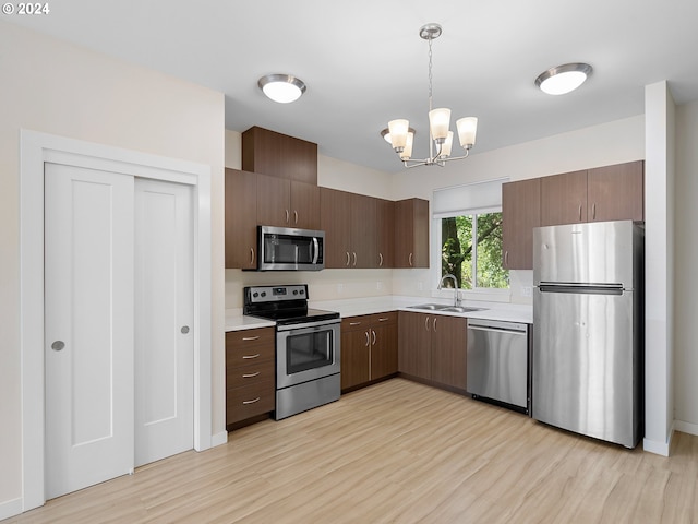 kitchen featuring sink, hanging light fixtures, a notable chandelier, stainless steel appliances, and light hardwood / wood-style floors