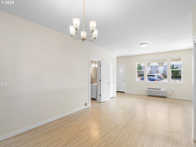 unfurnished living room featuring a chandelier, light hardwood / wood-style floors, and an AC wall unit