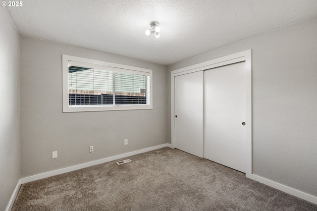 unfurnished bedroom with a closet, visible vents, carpet flooring, a textured ceiling, and baseboards