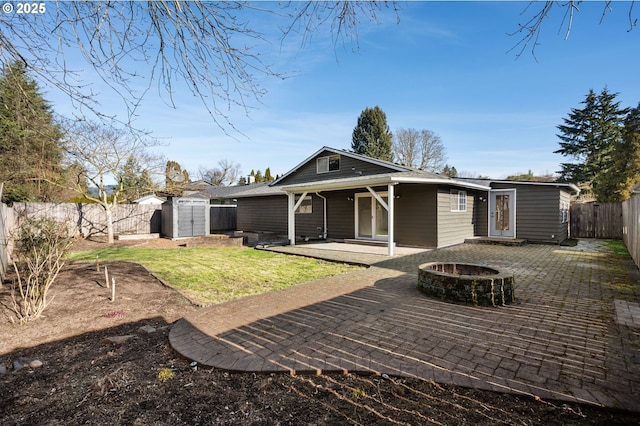 rear view of property featuring a fenced backyard, a fire pit, an outdoor structure, a storage unit, and a patio area