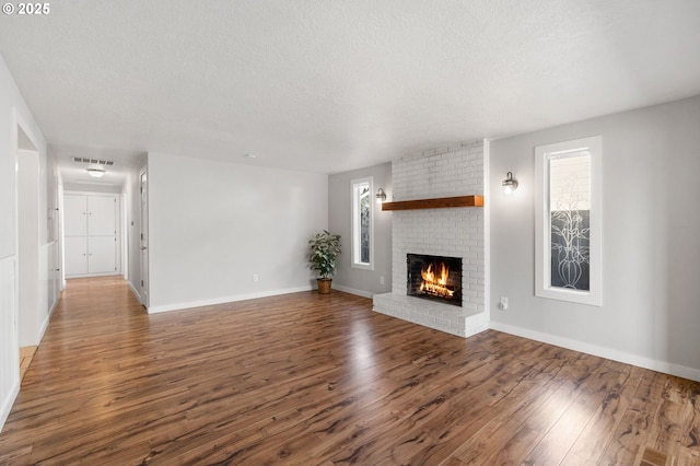 unfurnished living room with a textured ceiling, a brick fireplace, dark wood finished floors, and baseboards