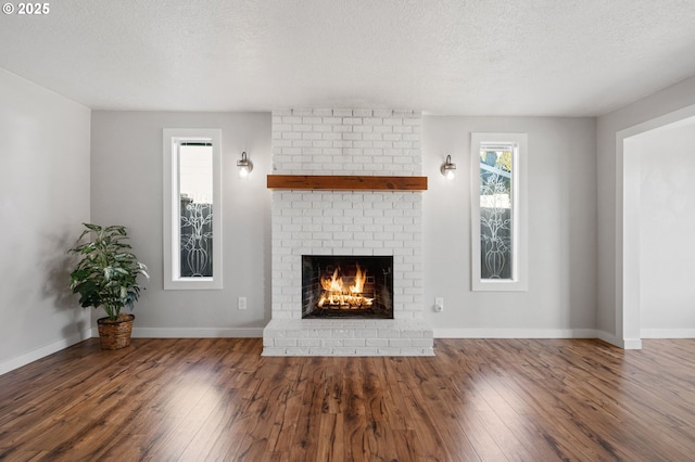 unfurnished living room with a brick fireplace, a textured ceiling, baseboards, and wood finished floors