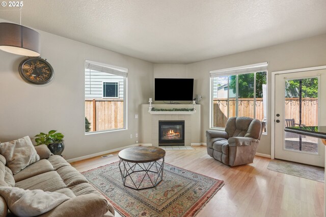 503 NW Hertel St, Hillsboro, OR 97124 - living room with light wood finished floors, a tile fireplace, baseboards, and a textured ceiling