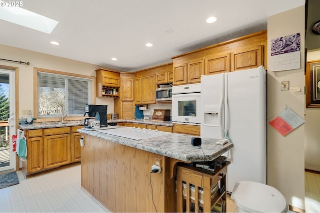 kitchen featuring white appliances, a kitchen bar, recessed lighting, a sink, and a skylight