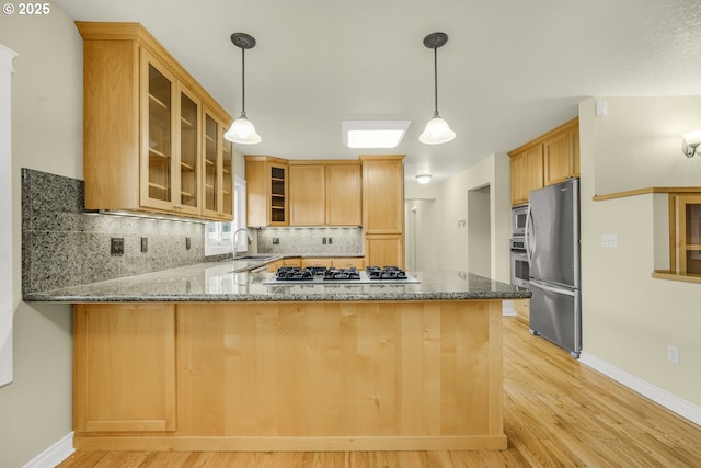 7307 SW Capitol Hwy, Portland, OR 97219 - kitchen with appliances with stainless steel finishes, a peninsula, stone countertops, decorative backsplash, and light wood-style flooring