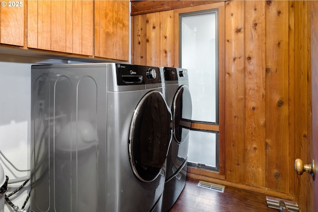 washroom featuring separate washer and dryer, dark wood-type flooring, cabinets, and wooden walls