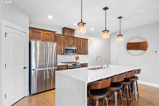 kitchen with hanging light fixtures, sink, an island with sink, appliances with stainless steel finishes, and tasteful backsplash